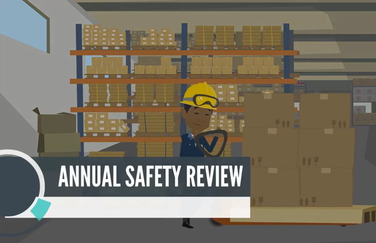 Animated course scene titled Annual Safety Review, showing a warehouse worker in a hard hat and safety goggles operating a pallet jack near stacked boxes