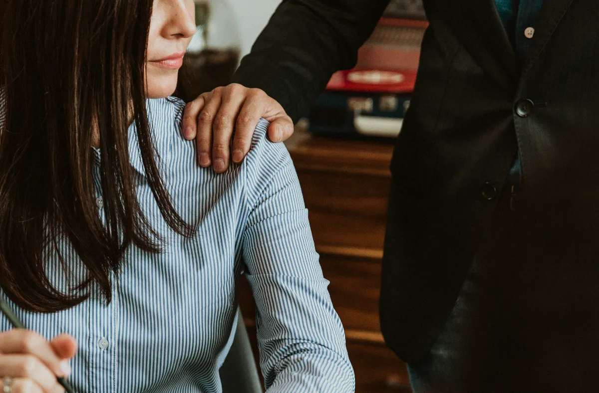 An unwelcome hand placed on a colleague's shoulder in an office setting, illustrating workplace sexual harassment